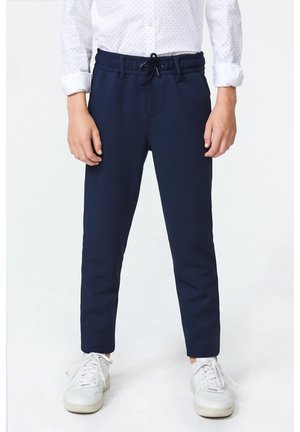 Pantaloni woven blu navy con vita regolabile, design tapered e tessuto testurizzato, abbinati a sneaker sportive bianche.