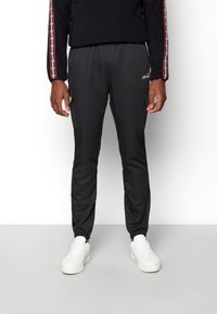 Černé sportovní tepláky s elastickým pasem, bočními kapsami a zúženými manžetami. Spárované s bílými teniskami.