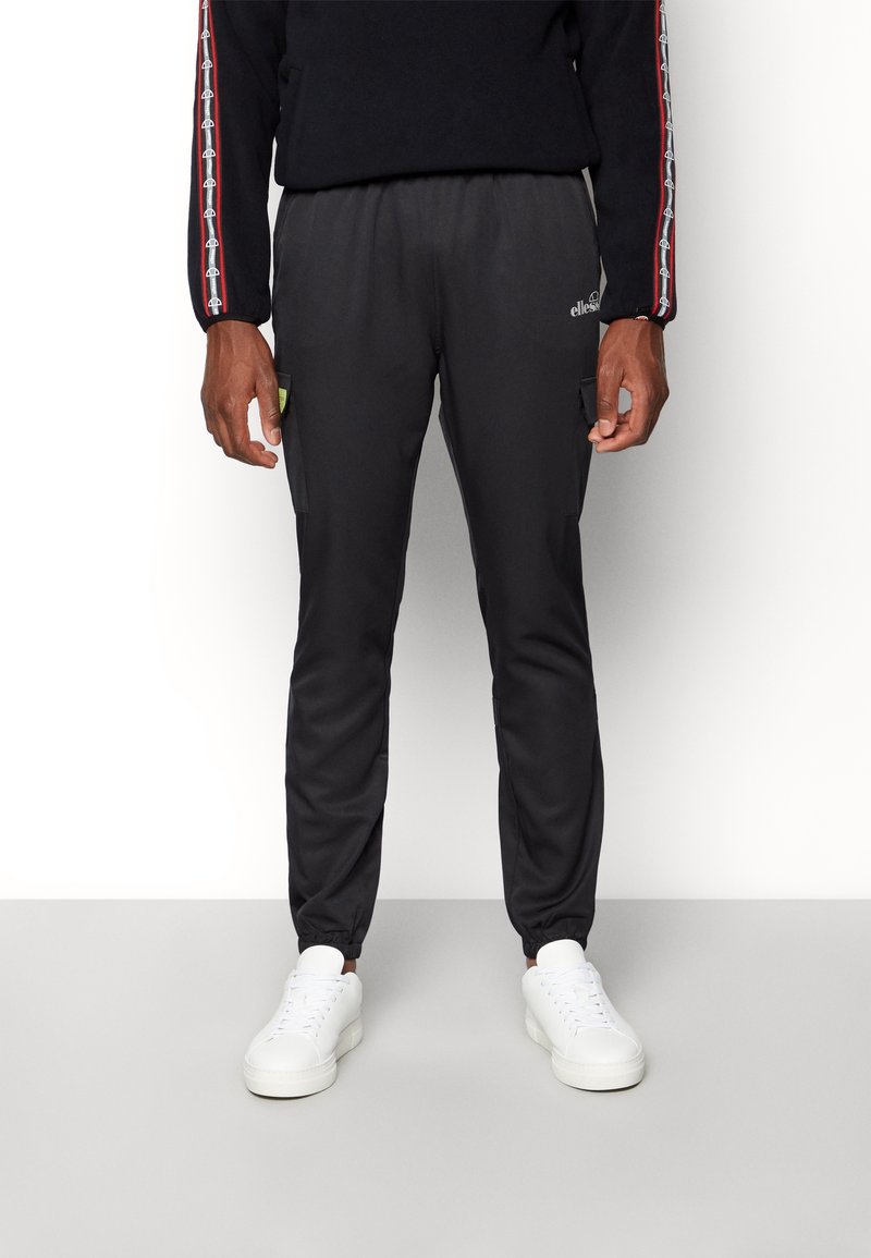 Černé sportovní tepláky s elastickým pasem, bočními kapsami a zúženými manžetami. Spárované s bílými teniskami.