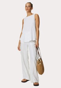 Haut sans manches en lin blanc et pantalon large, rehaussé d'un sac tressé marron. Texture lisse et coupe décontractée, offrant une esthétique légère et aérienne.