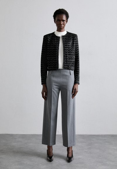 Black and white tweed jacket with a textured pattern, worn over a white crew-neck top and gray wide-leg trousers. Black pointed heels.
