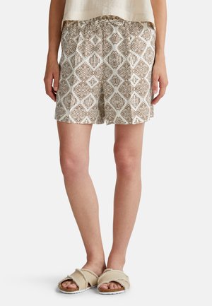 Shorts en coton avec une base crème et un motif abstrait de diamonds marron. Dotés d'une taille élastique et d'une coupe décontractée. Portés avec des sandales à glissière beiges.