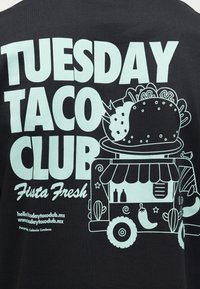 Σχέδιο μπλουζάκι με το κείμενο «Tuesday Taco Club Fiesta Fresh» και εικονογράφηση ενός τάκο πάνω σε ένα φαγάδικο φορτηγό διακοσμημένο με πιπεριές τσίλι και κάκτους.