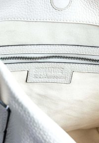 Interieur van een witte leren handtas met een ritsvak, textuurmateriaal en een merklabel dat is geperst op een stoffen patch.