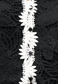 Μαύρο δαντελένιο ύφασμα με λουλουδάτα μοτίβα και κεντρική λευκή δαντέλα με μαύρα κουμπιά.