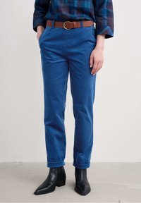 Sinised puuvillased püksid otse lõikega, millel on keeratud sääred ja pruun nahkvöö. Kombineeritud mustade ankle'ite saapadega.