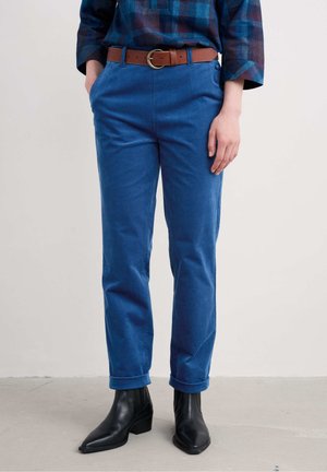 Blauwe katoenen broek met een rechte pasvorm, voorzien van opgerolde boorden en een bruine leren riem. Geland op zwarte enkellaarzen.