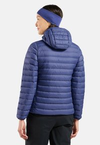 Steppjacke in Tiefblau mit gesteppter Optik, Kapuze und elastischen Bündchen. Getragen mit einem passenden blauen Stirnband.