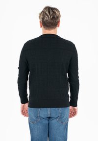 Czarny sweter o fakturze z kwadratowym wzorem, z prążkowanymi mankietami i dołem, noszony z niebieskimi dżinsami, widok od tyłu.