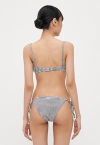 Fekete-fehér kockás bikini vékony pántokkal, állítható oldalszíjakkal és fitted szabással. Simább anyag és minimális fémből készült tartozék.