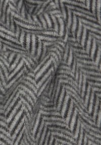 Tissu gris affichant un motif en chevrons avec des accents noirs, présentant une apparence douce et texturée ainsi qu'une arrangement plié et drapé.