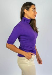 Paars coltrui met korte mouwen, aansluitend ontwerp, gemaakt van soepel materiaal, gecombineerd met lichtcrème kleurige trousers.