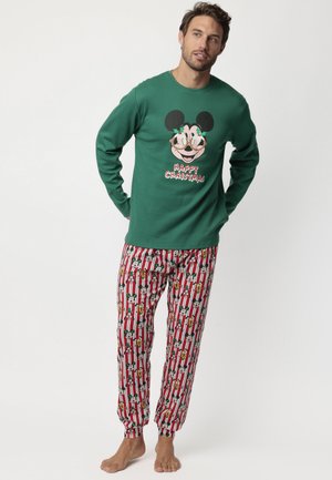 Hombre con camiseta de manga larga verde con diseño festivo de Mickey Mouse y texto "Feliz Navidad", combinado con pantalones de pijama de rayas rojas y blancas con patrón de Mickey.