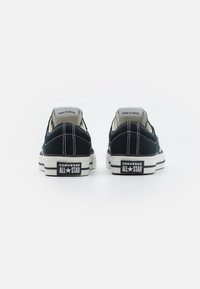 Černé plátěné tenisky s nízkým střihem, bílé gumové podrážky a kontrastním prošíváním. Na patě se nachází značka "Converse All Star".