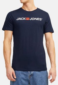 Navy blue cotton t-shirt featuring short sleeves, round neck, and white text logo "JACK & JONES" with an orange accent on the chest.