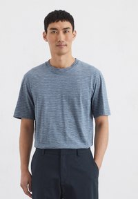 Gestreiftes kurzärmliges T-Shirt in verschiedenen Blautönen, mit einem runden Ausschnitt und einer lässigen Passform, kombiniert mit dunklen Hosen.
