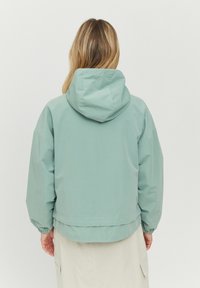 Ljusgrön, huva jacka med avslappnad passform, elastiska ärmslut och fåll som når precis ovanför höfterna. Slät, vattenavvisande tyg.