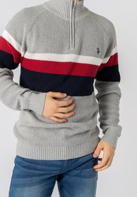 Šedý pletený svetr s zipovým límcem, který má horizontální pruhy v červené, bílé a námořnické modré. Hladké manžety a lem; středně těžká textura.