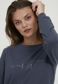 Felpa a maniche lunghe blu navy con una texture morbida, caratterizzata da un design script sottile "Eleganza Casual" sul davanti.