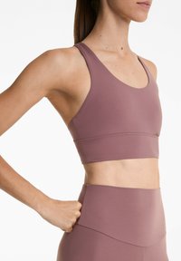 Mauve sportbh met brede bandjes en een ronde halslijn, met een gladde textuur en een horizontale naaddetail op de band.