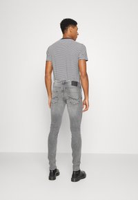Jeans ajustados grises con dos bolsillos traseros y una etiqueta de cuero negra, combinados con una camiseta a rayas en blanco y negro y botas negras.
