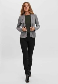 Šedý blazer přes tmavě zelený top, spárovaný s černými úzkými kalhotami. Blazer má štíhlý střih a klopové límce.