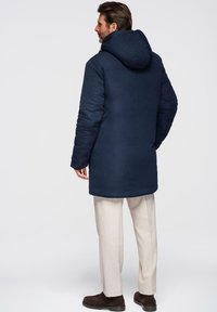 Marineblauwe gewatteerde jas met een capuchon, met een rechte snit, lange mouwen en een gladde textuur. De achterkant vertoont geen opvallende hardware of accenten.
