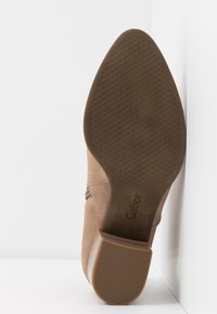 Brązowy zamszowy but na niskim obcasie, z teksturowaną gumową podeszwą i płaskim przodem. Wnętrze ma subtelne wytłoczone logo.