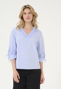 Hellbluse mit Streifen, Rüschen am V-Ausschnitt und dreiviertellangen Ärmeln, die an den Manschetten Bänder haben; glatte Stofftextur.