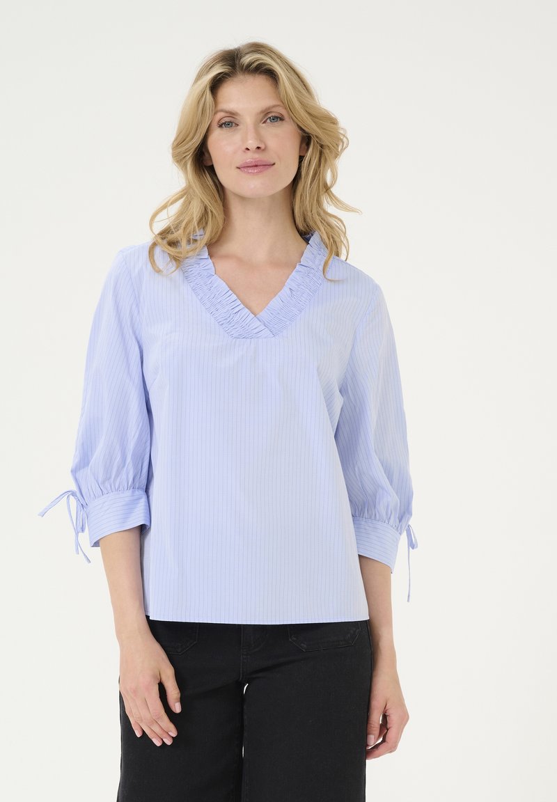 Hellbluse mit Streifen, Rüschen am V-Ausschnitt und dreiviertellangen Ärmeln, die an den Manschetten Bänder haben; glatte Stofftextur.