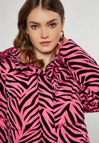 Roze pufferjack met een zwart zebra-streep patroon, met een capuchon en een ritssluiting. De stof heeft een glanzende textuur en een doorgestikt ontwerp.