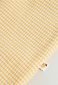 Geltoni ir balti dygsniuoti audiniai su maža etiketė, kurioje pavaizduotas persiko piešinys ant šviesios fono.