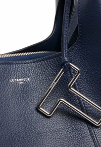 Borsa a tracolla in pelle blu navy con superficie texturizzata, zip argentata e un accent decorativo metallico geometrico attaccato alla tracolla.