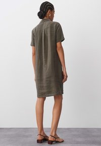 Kurzes, olivgrünes Leinenkleid mit lockerer Passform, ausgestattet mit einem Kragen mit Knopfleiste und einer Schulternaht hinten. Flaches, offenes Rückendesign.