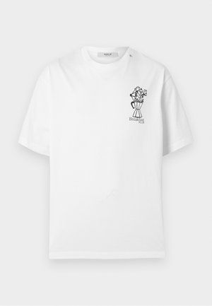 T-shirt bianca a maniche corte con piccolo disegno a linee nere di una caffettiera che tiene fiori e testo "Breakfast Klub" sul petto a sinistra.