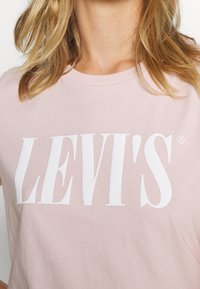 Ljust rosa bomullströja med en framträdande vit "LEVI'S"-logotyp. Rund halsdesign, korta ärmar och mjuk textur. Enkel och avslappnad stil.