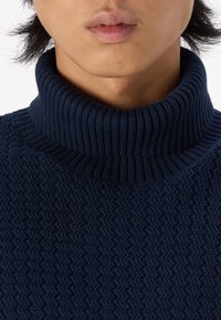 Suéter de punto azul marino con cuello alto de canalé, patrón en zigzag texturizado y tela suave y elástica.