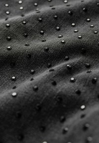Tissu noir avec une surface texturée, orné de petits clous noirs brillants disposés de manière uniforme, créant un contraste de textures.