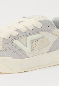 Sneaker in suede grigio chiaro con lacci crema, dotato di un dettaglio testurizzato del logo e piccole perforazioni sul lato. Suola in gomma.