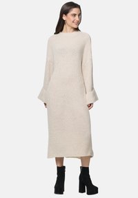 Kremowa sukienka dzianinowa z długimi rękawami i luźnym krojem, z prążkowanym dekoltem i mankietami w kształcie dzwonów, sięgająca do połowy łydki.