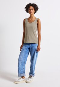 Tajt passande ärmlös linne i olivgrön bomull med en lätt V-ringning. Parat med ljusblå denimjeans med uppvikt nederkant och vita sneakers.