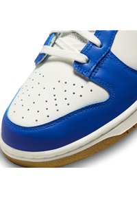 Blue and white sneaker, featuring a smooth leather upper, perforated toe box, white laces, and a textured gum rubber sole.