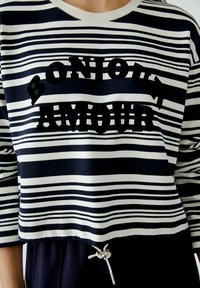 Marineblauwe en witte gestreepte sweatshirt met zwarte fluwelen tekst "BONJOUR AMOUR," voorzien van een trekkoord onderaan en een ronde halslijn.