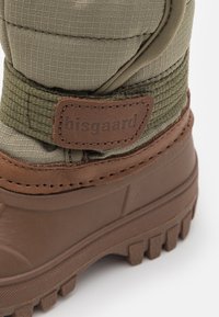 Hnědá gumová bota s texturovaným, olivově zeleným svrchním materiálem a hnědým koženým akcentem s logem "bisgaard". Silná podrážka s výrazným vzorem.