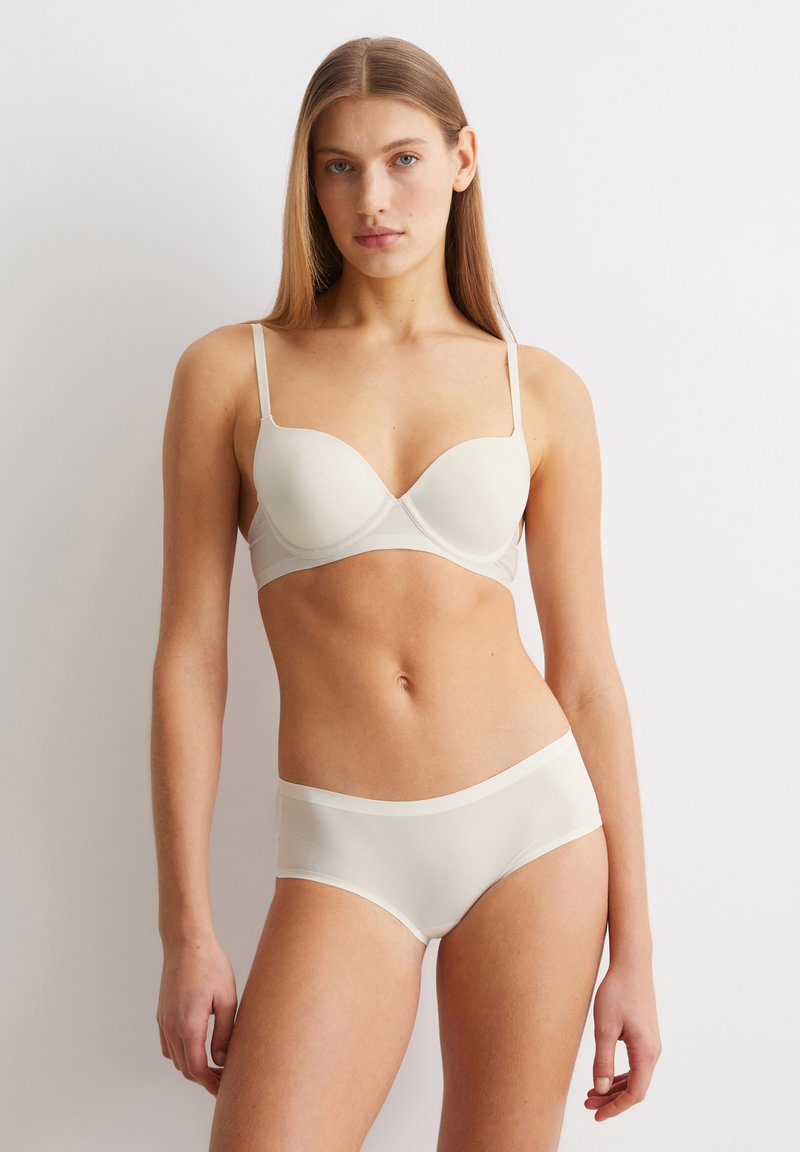 Lichtbeige lingerie set met een gepadded beha met verstelbare straps en een bijpassende slip, beide vervaardigd uit een gladde, zachte stof.