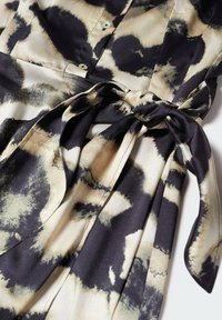 Robe boutonnée avec un motif abstrait noir, beige et crème, dotée d'une ceinture en tissu nouée à la taille.