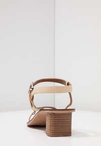 Beige klack-sandaler med bakrem och justerbar spänne. Har en träblockklack och en slät läderöverdel.