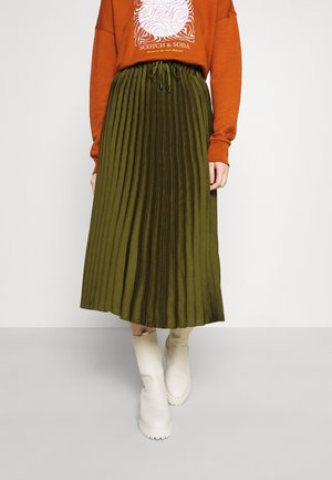 Jupe midi plissée vert olive avec une taille élastique et un cordon de serrage, associée à un pull couleur rouille et des bottines crème.
