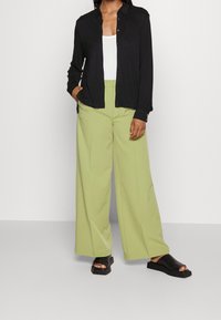 Svart skjorta med knappar, vit linne, ljusgröna vida byxor och svarta sandaler. Slät tyg med avslappnad passform.