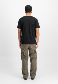 Camiseta negra de algodón y pantalones cargo verde oliva. La camiseta tiene cuello redondo; los pantalones cuentan con bolsillos laterales y un ajuste holgado.
